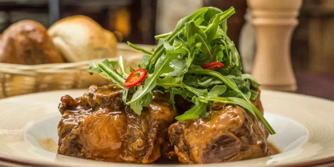 Delicioso rabo de toro en salsa, coronado con rúcula fresca y rodajas de chile. Una receta que conquista paladares.