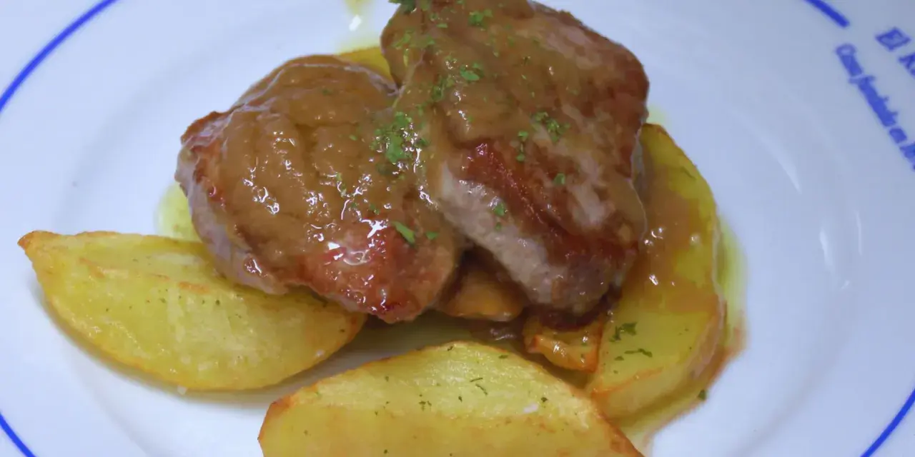 Solomillo jugoso con salsa de whisky sobre patatas gajo en un plato blanco.