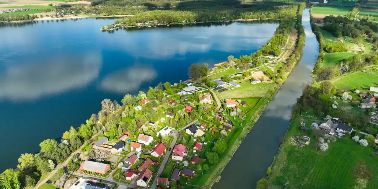 Pławniowice jezioro otoczone zielenią i domkami letniskowymi, z kanałem wodnym biegnącym wzdłuż brzegu.