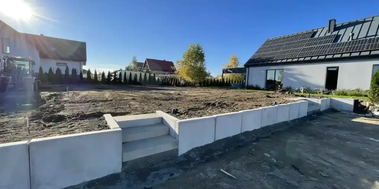 Nowe schody i betonowy murek to co zamiast muru oporowego, otaczają plac budowy domu z panelami słonecznymi.