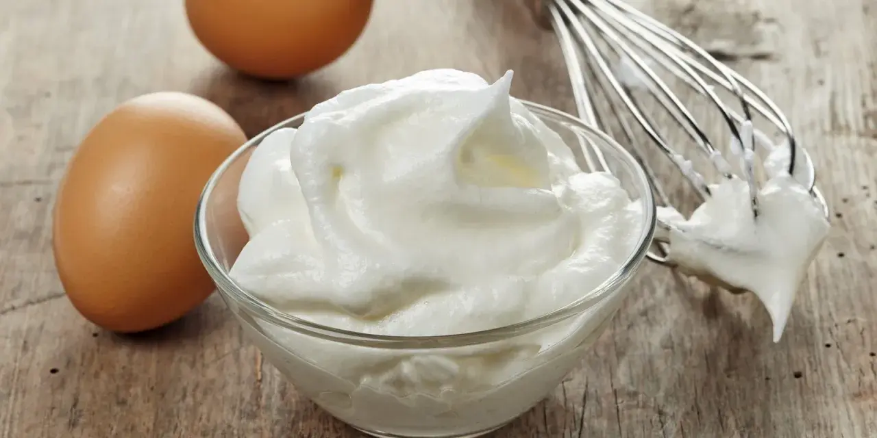 Zwei Eier und ein Schneebesen neben einer Schüssel mit luftigem Eischnee, der nicht fest wird.
