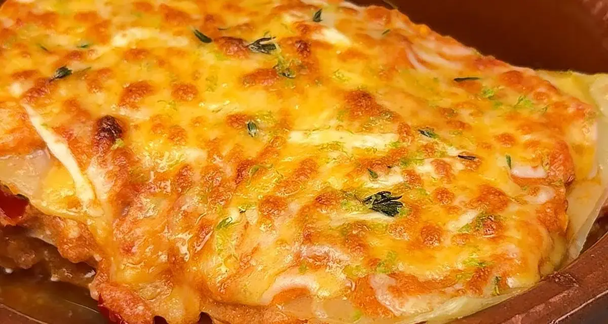 Deliciosa lasaña de atún gratinada con queso dorado y hierbas frescas, servida en una cazuela de barro.