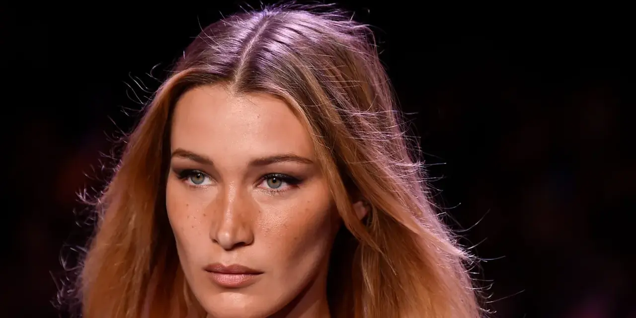 Primo piano di una modella con capelli biondi mossi e occhi verdi penetranti. La sua espressione è enigmatica, quasi a chiedersi chi è la donna più bella del mondo.