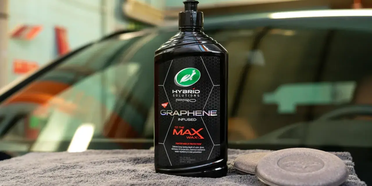 En flaska Turtle Wax Hybrid Solutions Pro Graphene Infused To The Max Wax står på en grå trasa bredvid två appliceringsdynor.