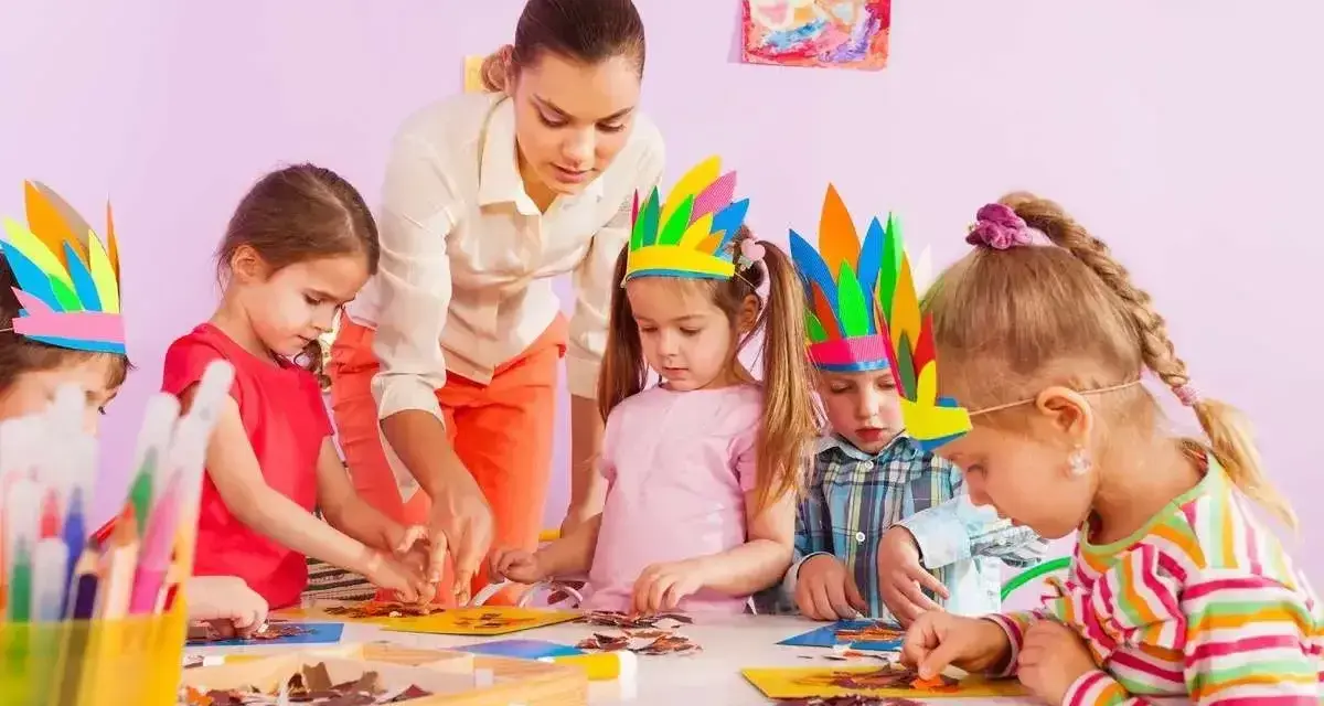 Nauczycielka pomaga dzieciom w tworzeniu pióropuszy. Jedno z dzieci, 4-latek, nie chce się bawić z dziećmi, ale skupia się na pracy.