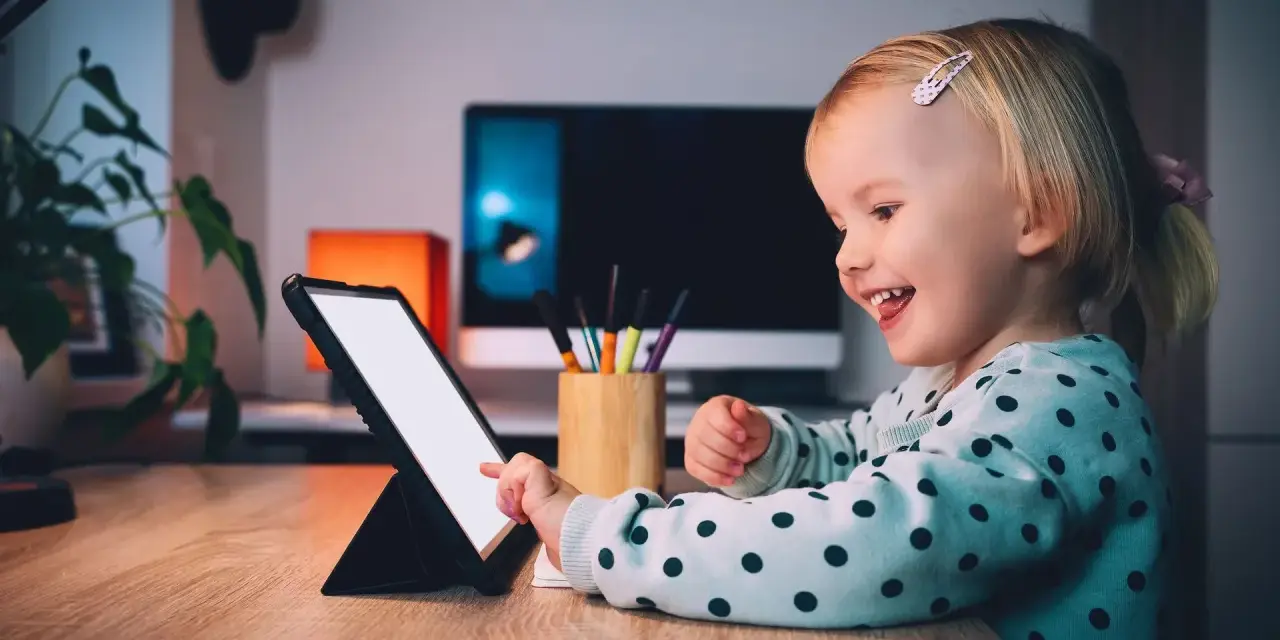Uśmiechnięta dziewczynka ogląda ulubionych youtuberów dla dzieci na tablecie.