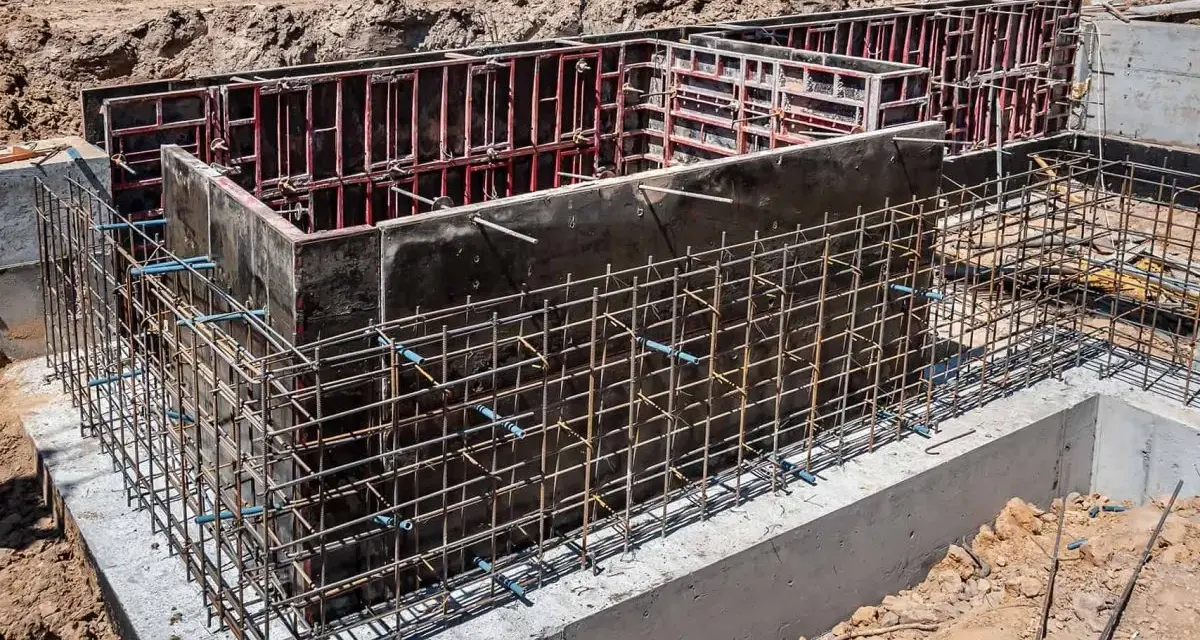 Siatka zbrojeniowa otacza betonowe szalunki, tworząc solidne zbrojenie ściany fundamentowej.