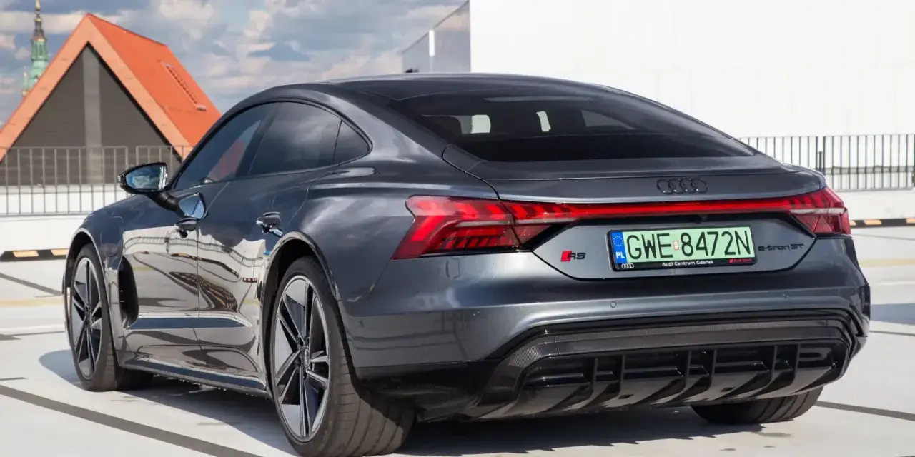 Tył ciemnoszarego Audi RS e-tron GT na parkingu, z widocznymi światłami i tablicą rejestracyjną.
