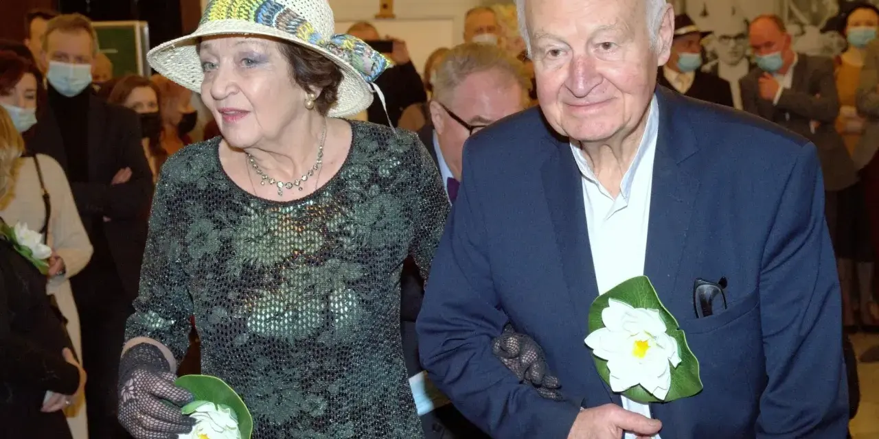 Ewa Dałkowska z synem Ksawerym, elegancko ubrani, z kwiatami w dłoniach, podczas uroczystości.