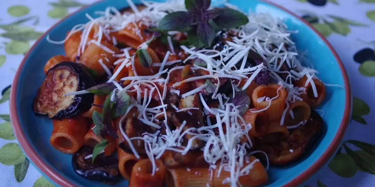 Pyszne danie pasta alla norma z makaronem rigatoni, bakłażanem w sosie pomidorowym i posypane startym serem.
