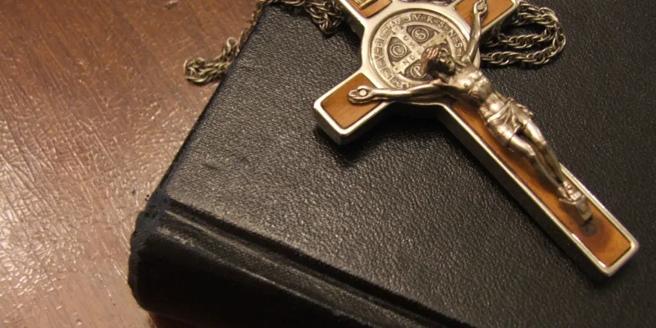 Krzyż z Jezusem i łańcuszek na czarnej księdze, symbol wiary i nadziei, narzędzia, które mógłby mieć przy sobie egzorcysta.