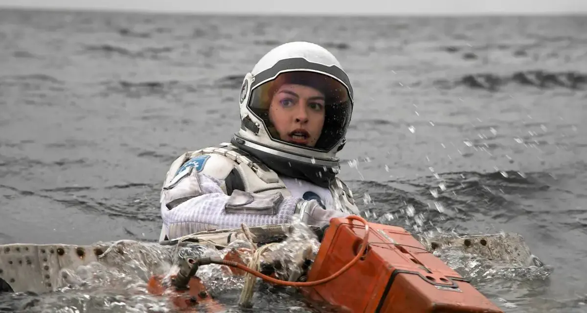 Astronautka w skafandrze z filmu Interstellar 2 w wodzie, z pomarańczowym urządzeniem.