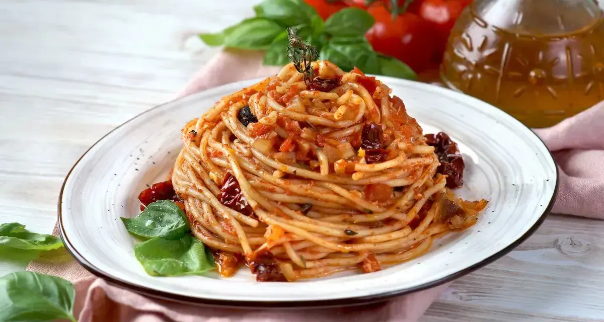 Un piatto di spaghetti conditi con un sugo rosso ricco di pomodori secchi, basilico fresco e un filo d'olio d'oliva.