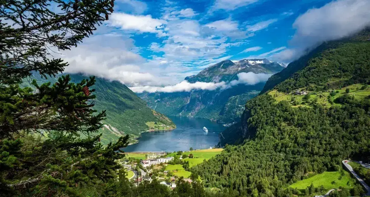 Majestatyczne fiordy Norwegii, z zielonymi zboczami gór, błękitnym niebem i statkiem wycieczkowym na wodzie.