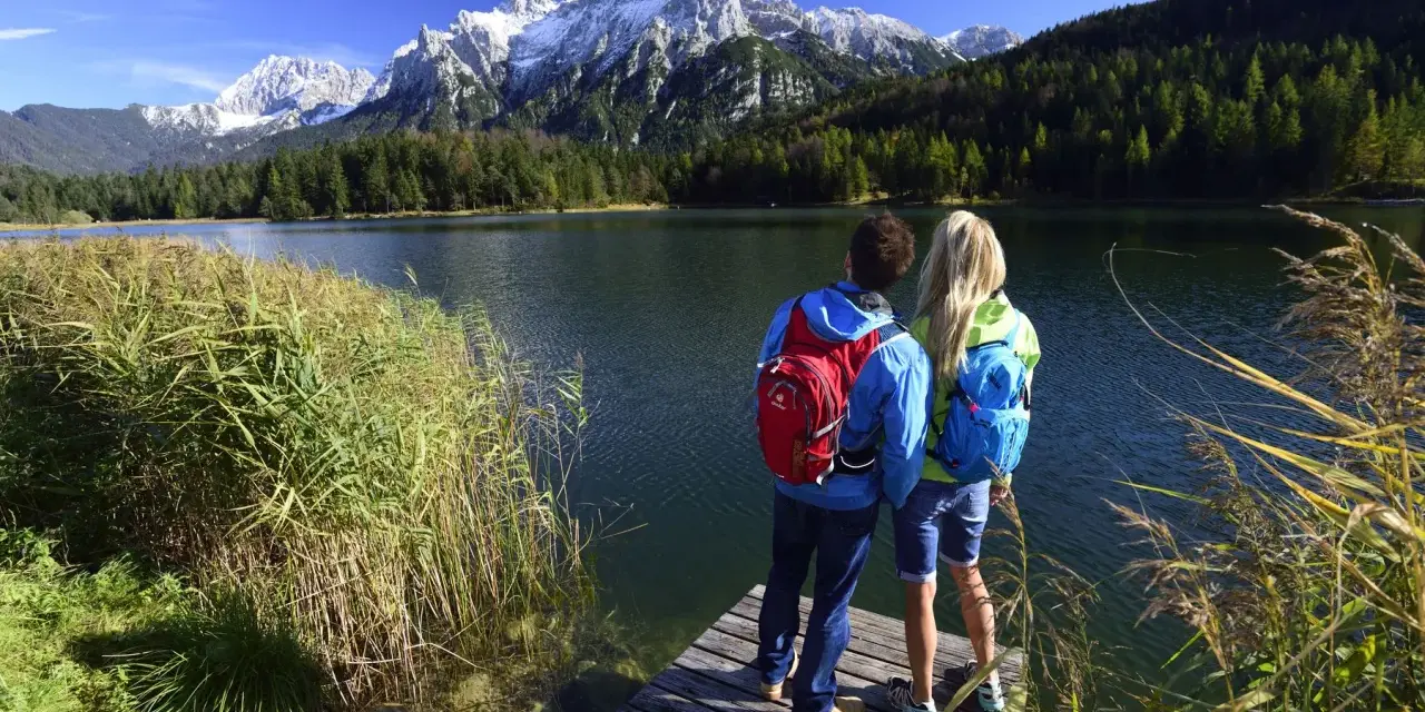 Ein Paar genießt die Aussicht auf die Berge bei Garmisch-Partenkirchen. Sie stehen auf einem Steg am See, bereit zum Wandern.