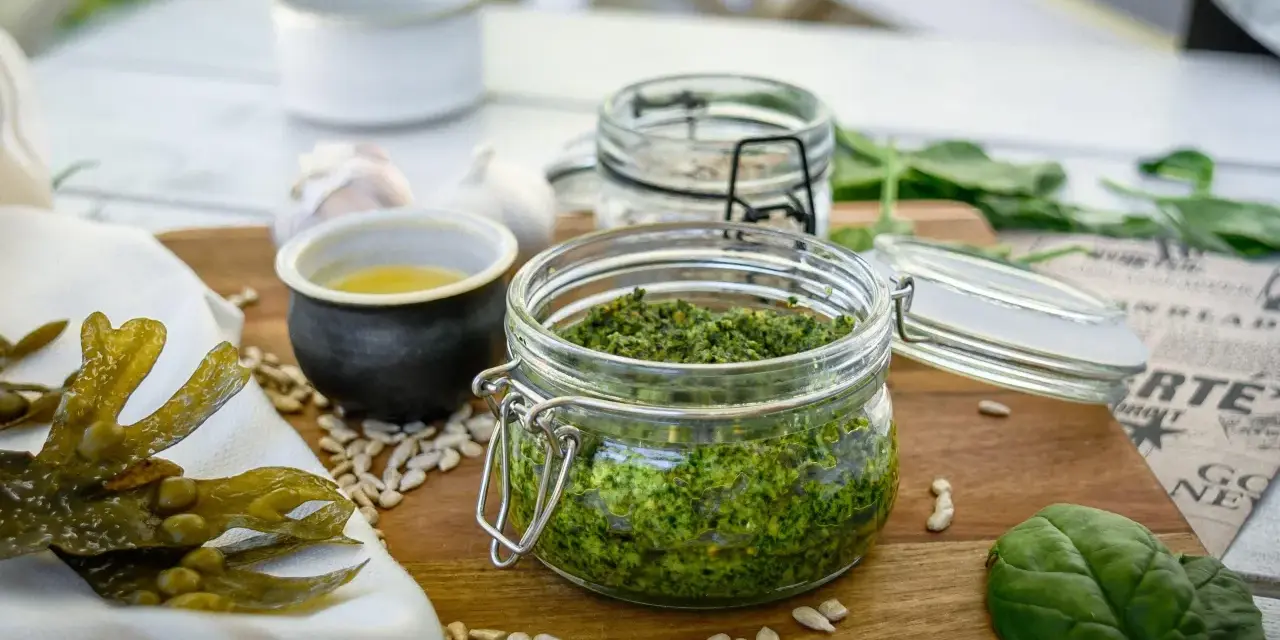 Frisches Pesto aus essbaren Algen der Nordsee, daneben Sonnenblumenkerne, Knoblauch und ein kleines Schälchen mit Öl.