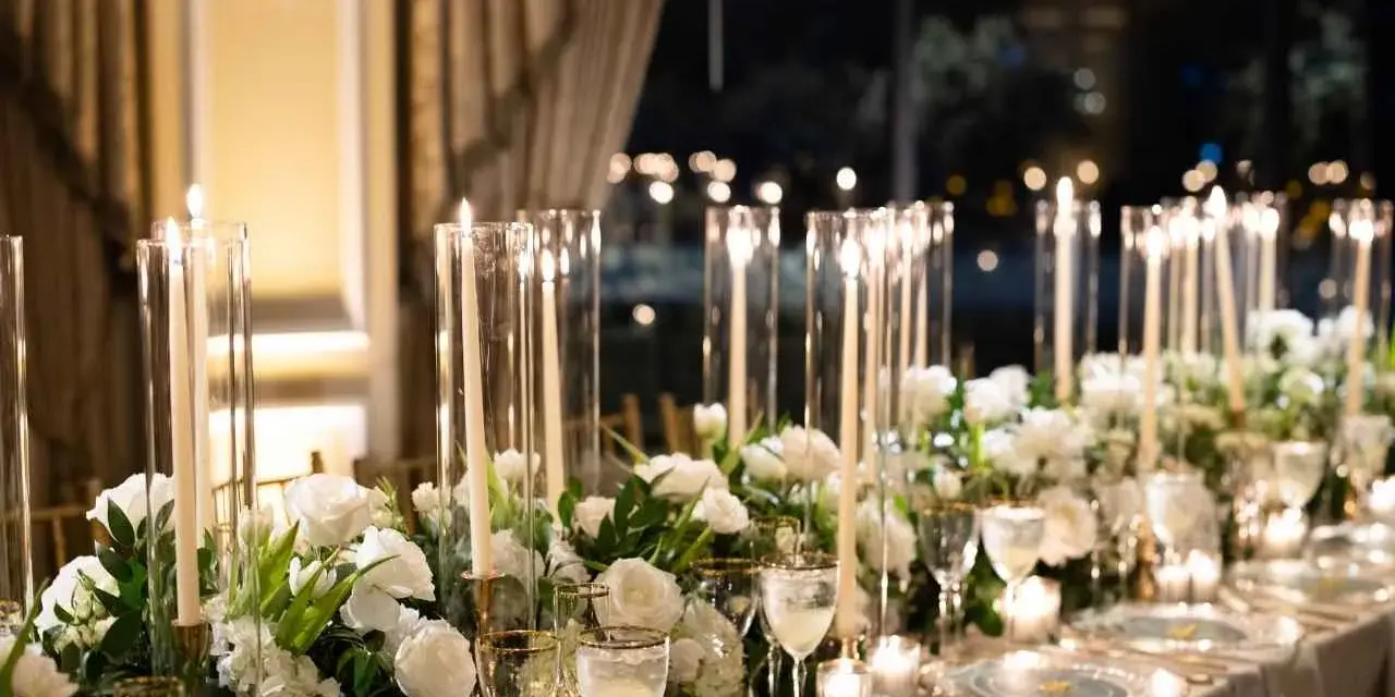 Eleganckie kwiaty na wesele zdobią stół, a wysokie świece w szklanych wazonach tworzą magiczny nastrój.