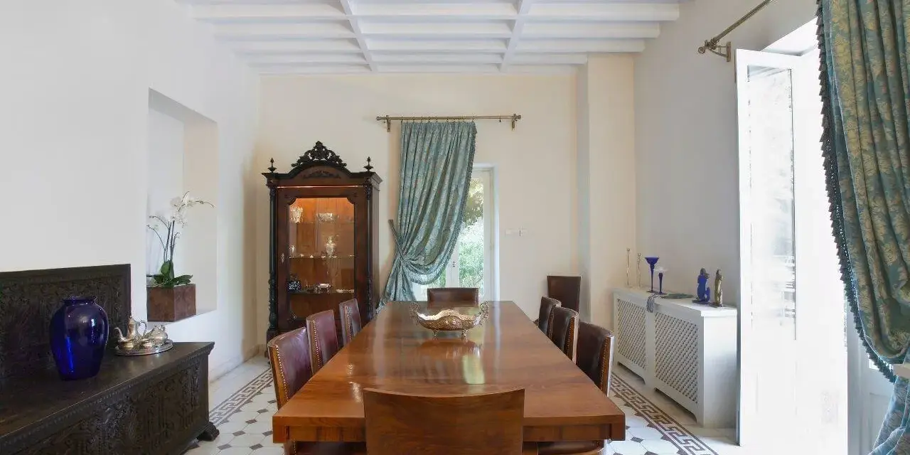 Elegancka jadalnia w stylu kolonialnym z drewnianym stołem, witryną i zdobioną skrzynią.