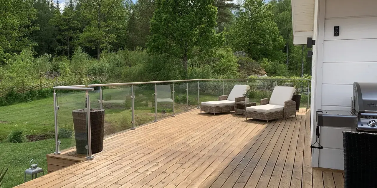 Nyligen oljad altan med solstolar och grill. Vacker utsikt över grönskande skog och en sommarhimmel.