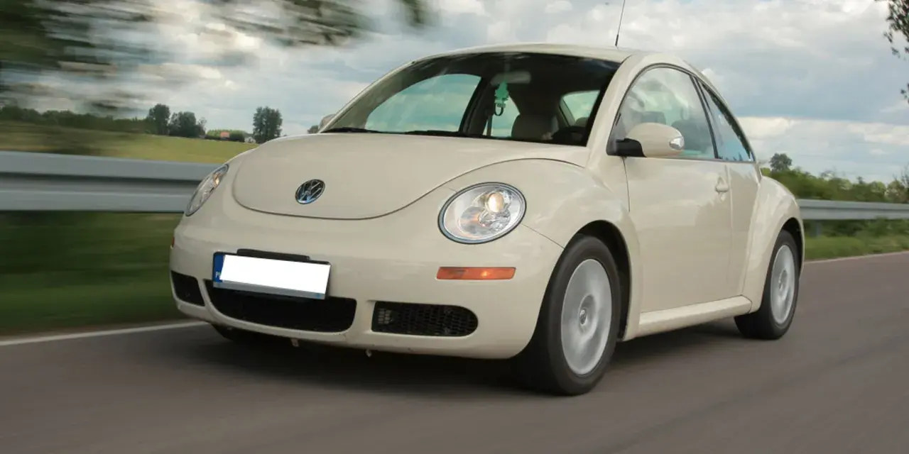 Jasny Volkswagen Beetle w ruchu na drodze, z rozmytym tłem.