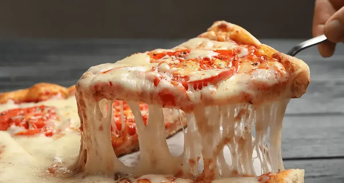 Rozciągający się, ciągnący ser na kawałku pizzy z pomidorami. Idealny przykład, jaki ser do pizzy wybrać, by uzyskać taki efekt.