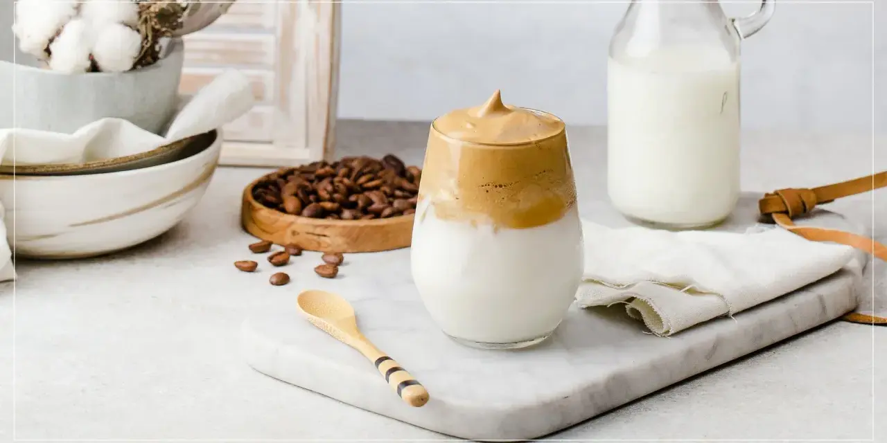 En krämig dalgona coffee med fluffigt skum, serverad med mjölk och kaffebönor.