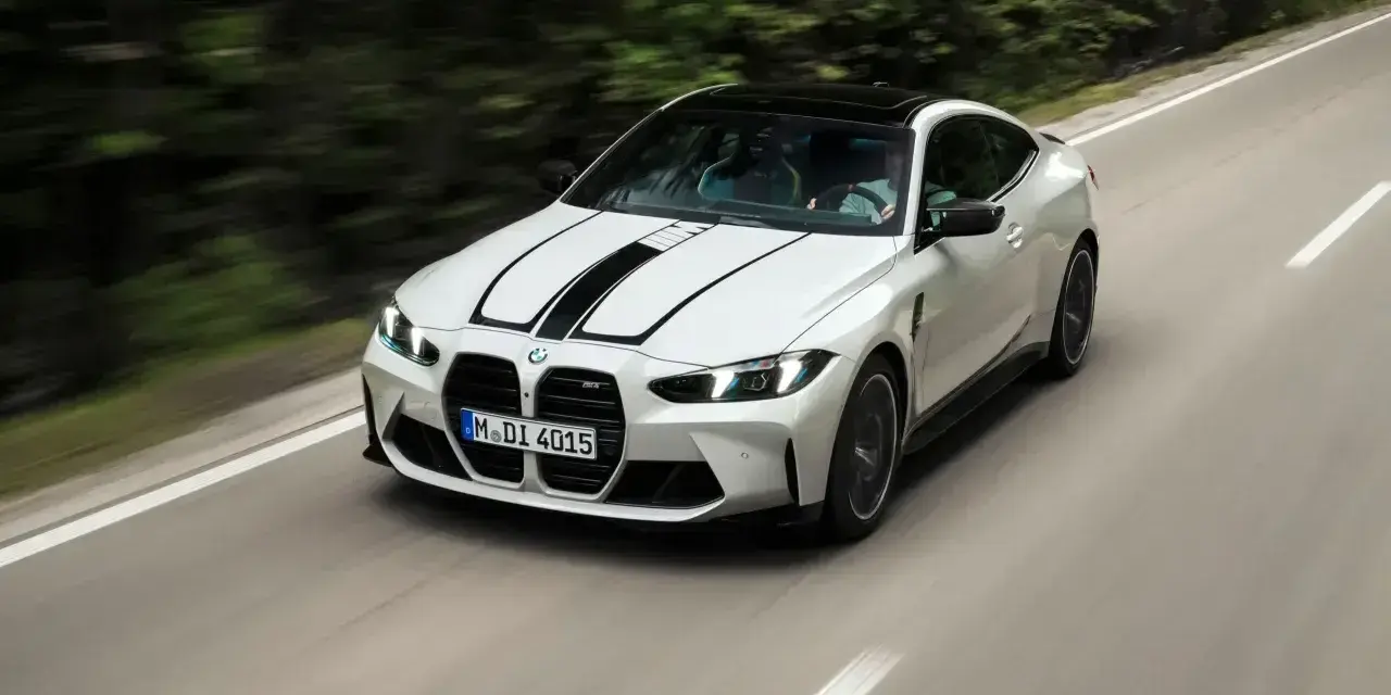 Białe BMW M4 z czarnymi pasami na masce pędzi po krętej drodze. Zastanawiasz się, ile kosztuje BMW M4?