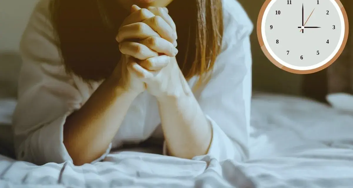 A woman is praying at 3am in the morning, her hands clasped tightly. The clock shows the early hour.