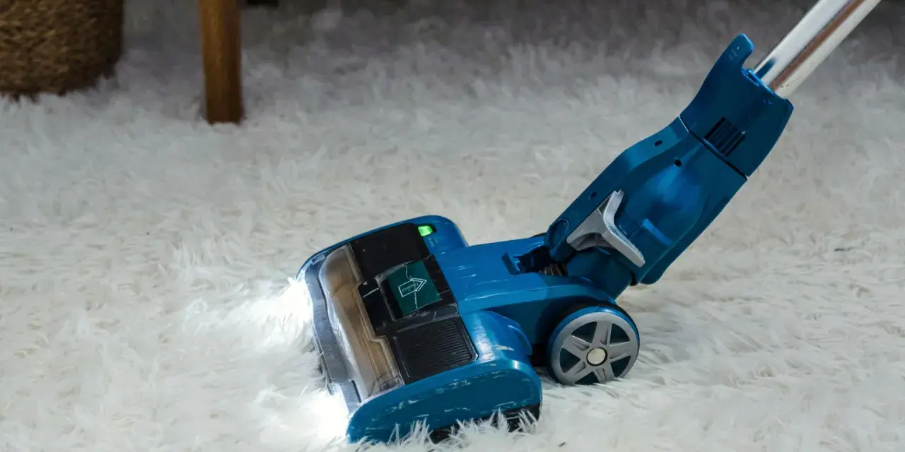 Blauer Staubsauger mit LED-Licht reinigt flauschigen Teppich. Die Leistung, wie viel Watt hat ein Staubsauger, ist entscheidend für die Saugkraft.