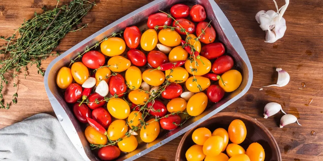 Pomodorini al forno rossi e gialli, aglio e peperoncino in una teglia, pronti per essere cotti.