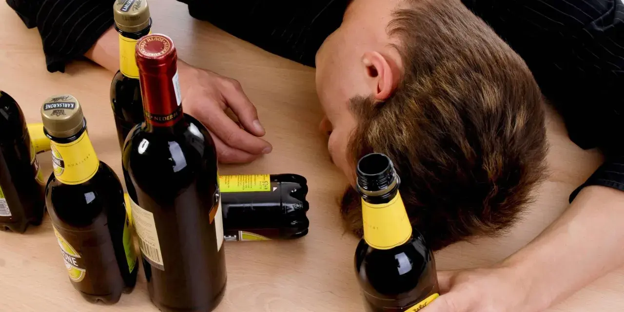 Ein Mann liegt bewusstlos auf einem Tisch, umgeben von leeren Flaschen. Der Gedanke, dass **Whisky gesund** sein könnte, ist hier wohl fehl am Platz.