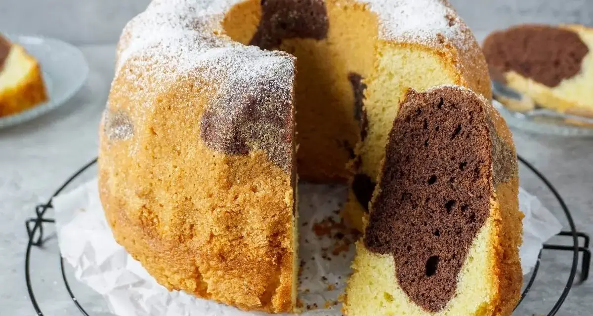 Saftiger Marmorkuchen, perfekt gebacken mit Ober-/Unterhitze oder Umluft, bestäubt mit Puderzucker. Ein Stück ist bereits angeschnitten.