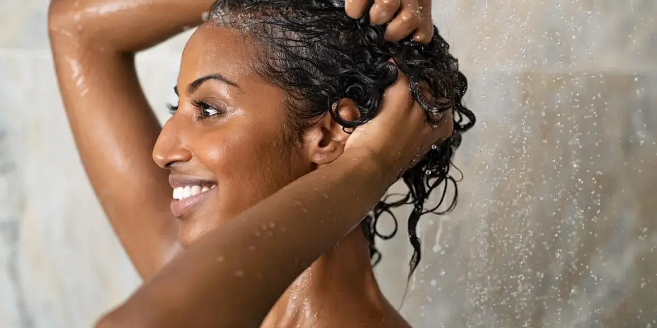 Frau wäscht sich unter der Dusche die Haare. Sie fragt sich, wie oft Haare waschen am besten ist.