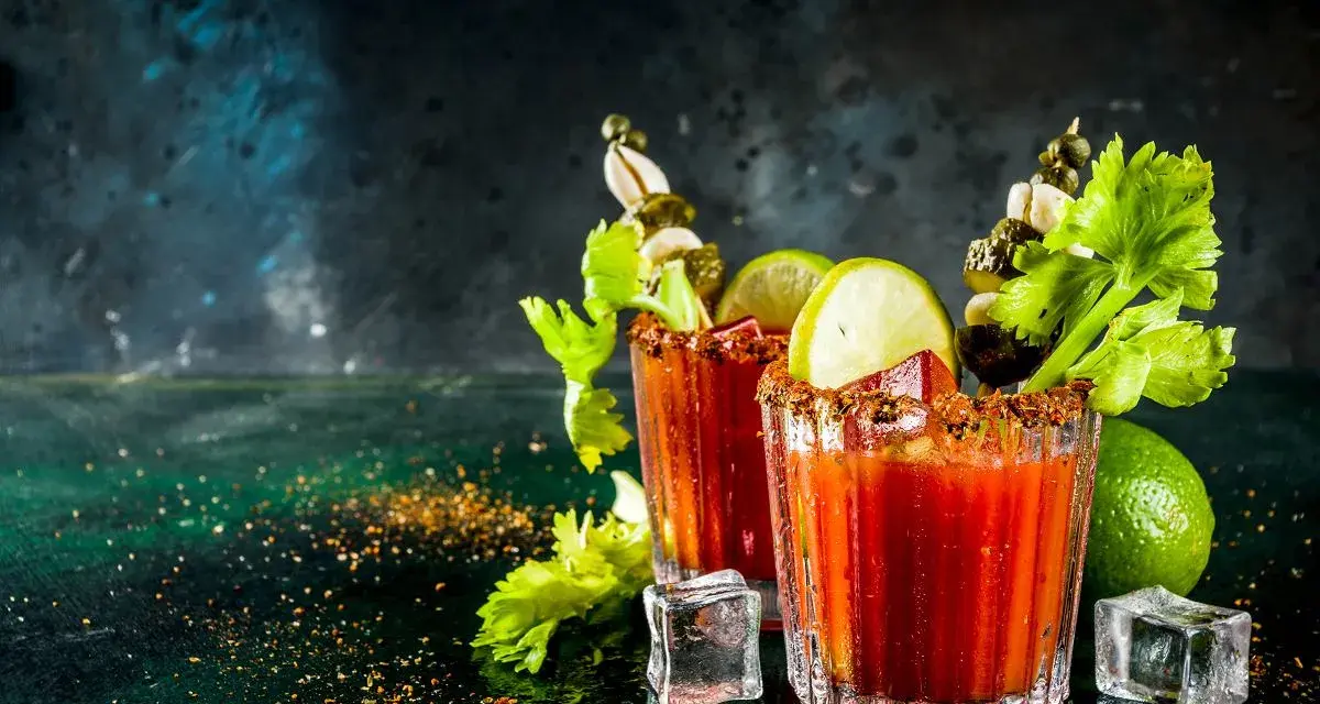 Dwa drinki Krwawa Mary z łodygami selera, limonką i piklami, ozdobione przyprawami i lodem.