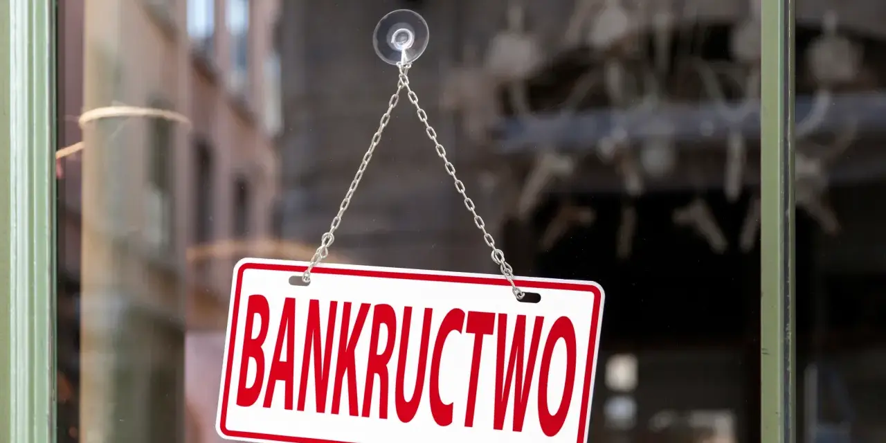 Tabliczka "BANKRUCTWO" wisząca na łańcuszku na szybie.
