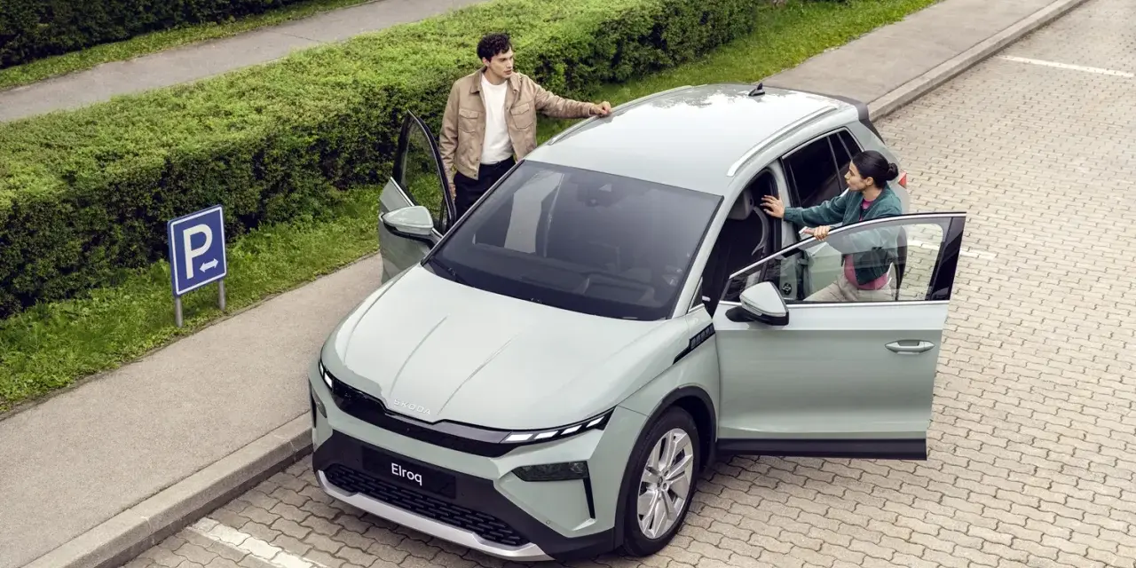 Jasnoszary elektryczny SUV Škoda Elroq z otwartymi drzwiami, obok którego stoją młoda kobieta i mężczyzna.