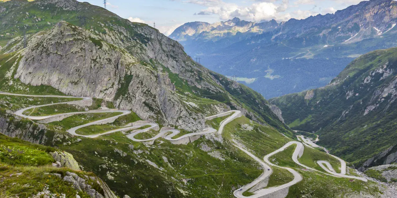 Strada tortuosa che sale sul passo Austria, circondata da montagne verdi e rocce imponenti.