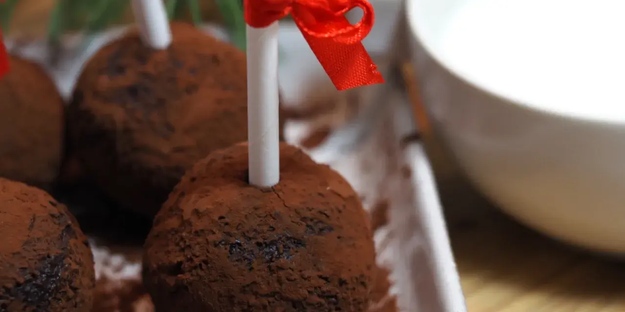 Chokladbollar på pinne, pudrade med kakao, redo att doppas i varm choklad. Röda band pryder pinnarna.