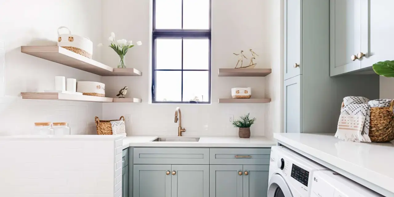 Stylish laundry room with mint cabinets, floating shelves, and a sink. This organized space shows how to organize laundry room with baskets and jars.