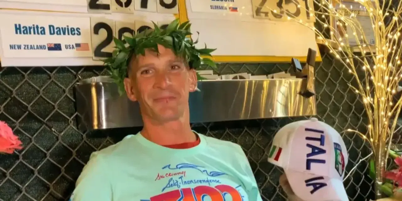 Vincitore con corona d'alloro, indossa una maglietta con scritto "3100" e un cappellino "ITALIA". Potrebbe essere un traguardo della ultramaratona più lunga del mondo.