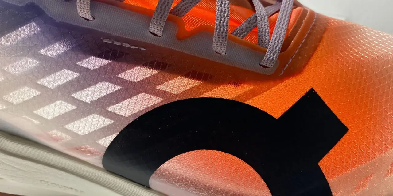 La tomaia di una scarpa da corsa arancione e viola con lacci grigi e un logo nero.