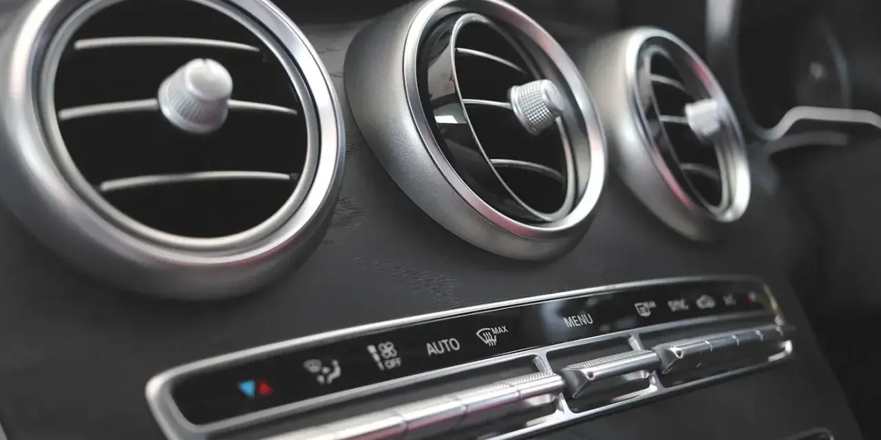 Trzy okrągłe nawiewy wentylacji w samochodzie, z pokrętłami do regulacji. Poniżej panel sterowania klimatyzacją, z przyciskami AUTO i MAX. Czekam na bardzo gorące powietrze z nawiewu.