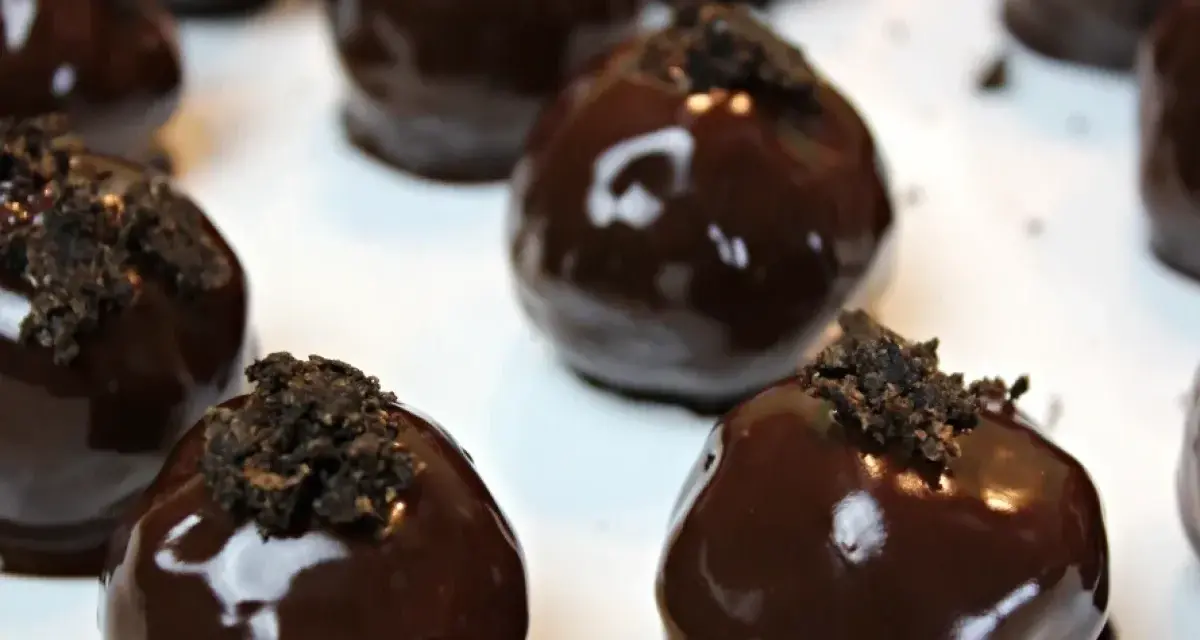 Deliziosi tartufini al cocco ricoperti di cioccolato fondente lucido, guarniti con briciole croccanti.