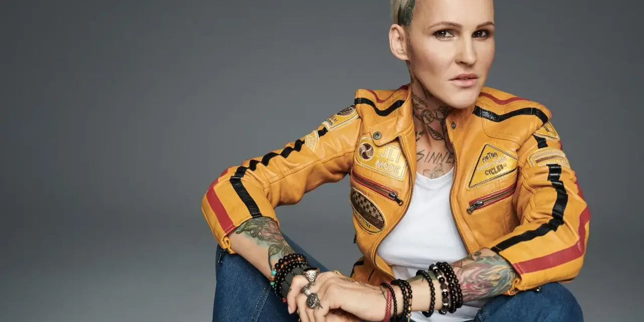 Agnieszka Chylińska w żółtej kurtce motocyklowej, z tatuażami i biżuterią. Jakby mówiła: "kiedyś do ciebie wrócę".