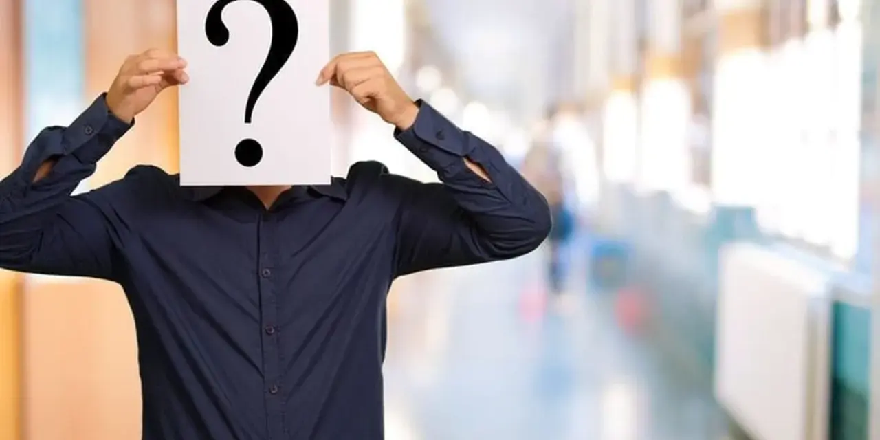 Un homme en chemise bleue cache son visage derrière un point d'interrogation. Une métaphore visuelle pour la quête : comment retrouver une personne sans son nom et prénom ?