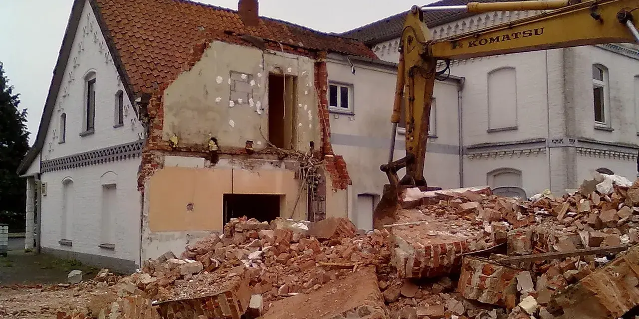Rozbiórka budynku w granicy działki. Koparka Komatsu pracuje przy gruzach.