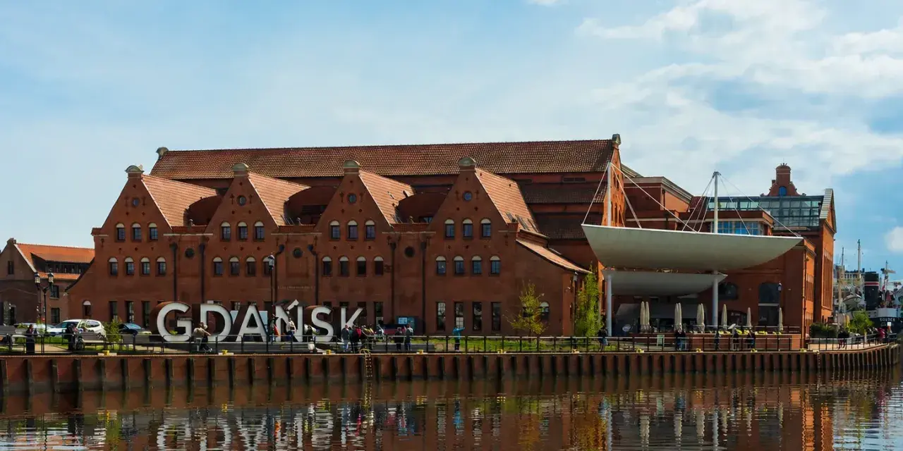 Gdańsk zwiedzanie: ceglane kamieniczki nad Motławą, wielki napis "GDAŃSK" i odbicie w wodzie.