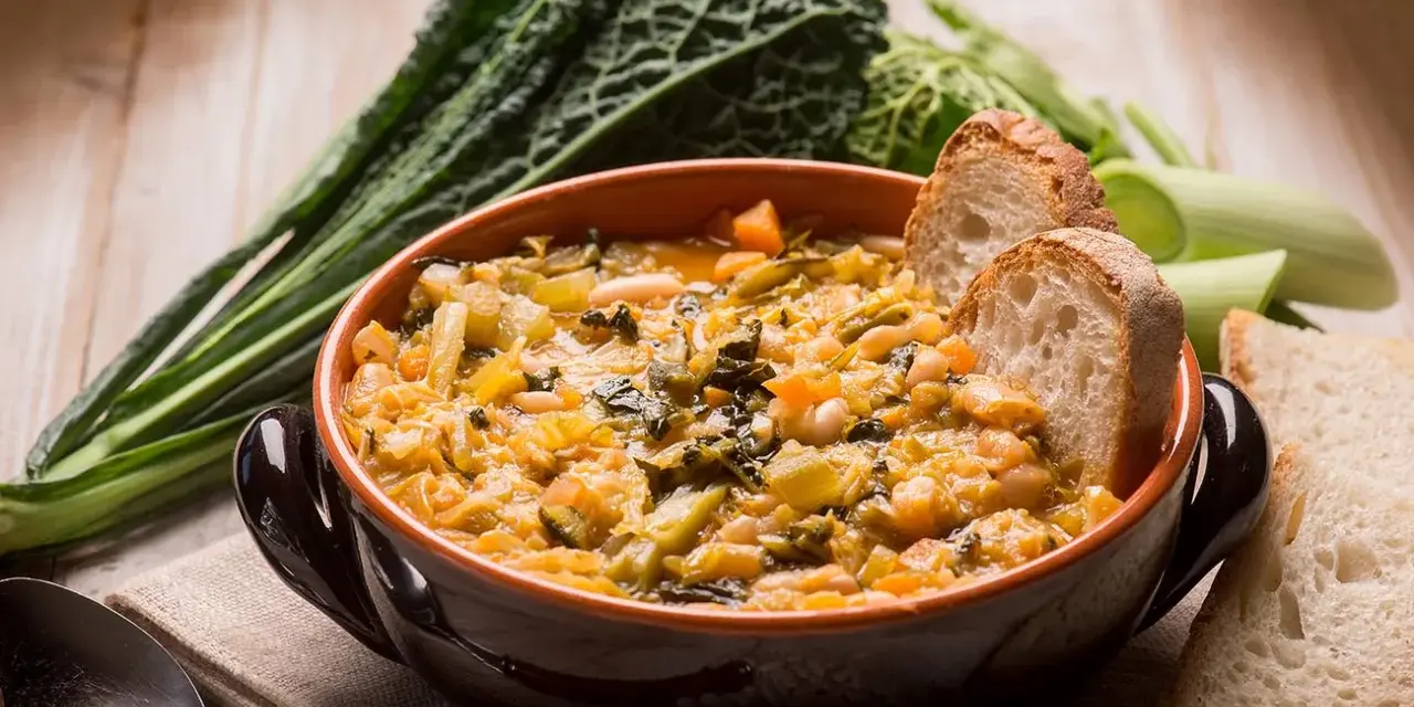 Una ciotola di ribollita fumante, ricca di verdure e fagioli, accompagnata da fette di pane tostato e cavolo nero.