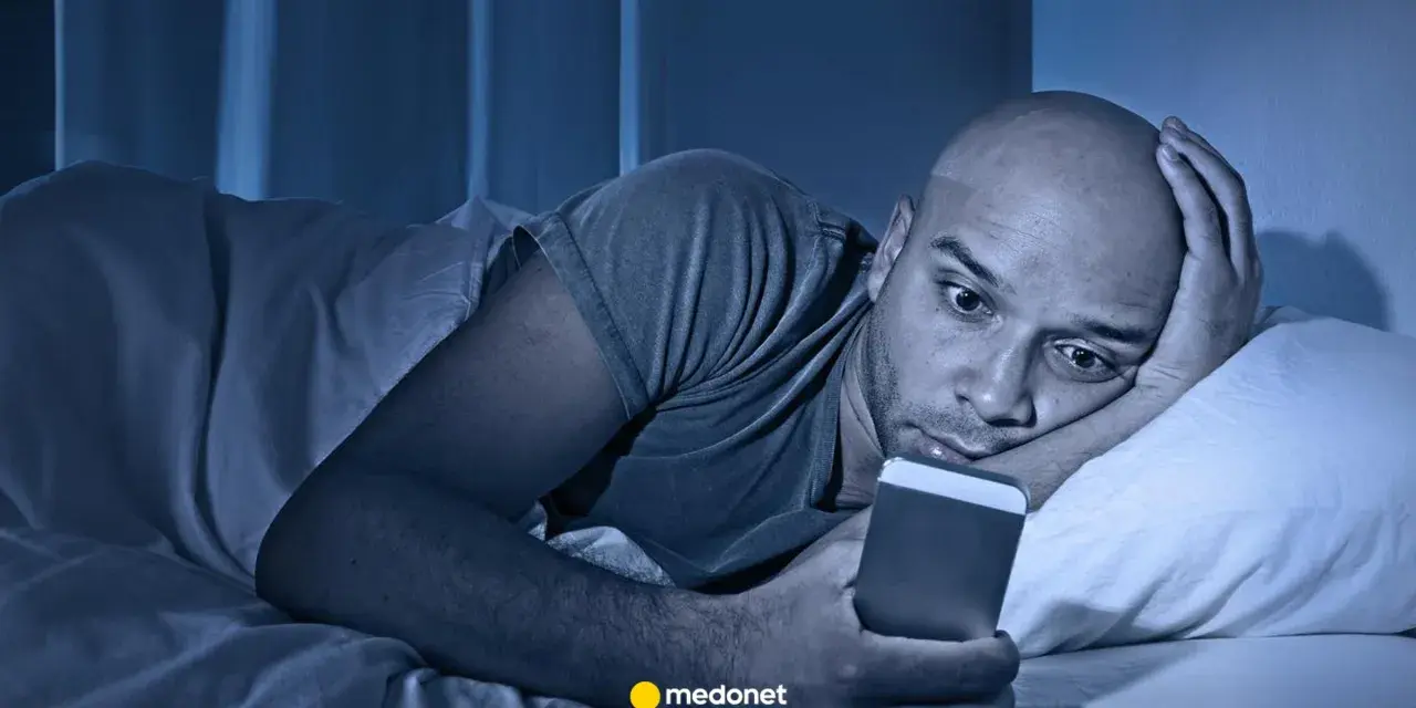 Mężczyzna leży w łóżku, wpatrując się w telefon. Czy to już obsesja?