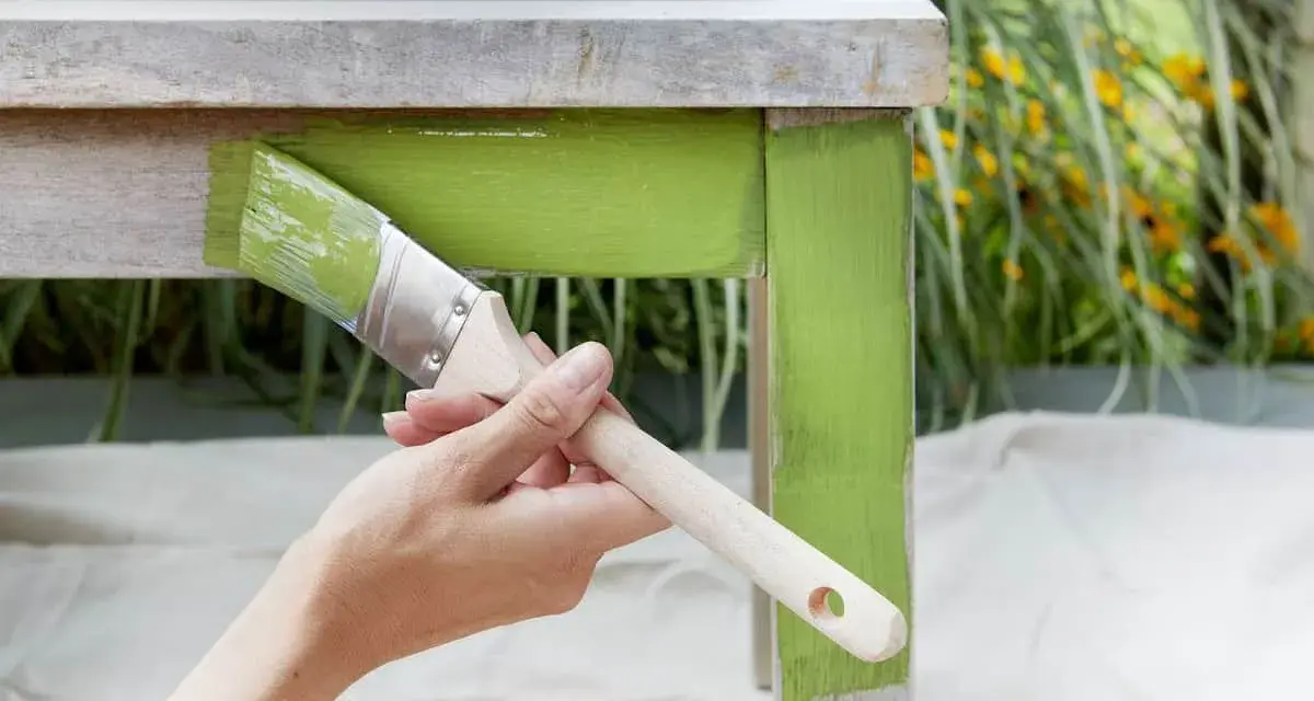 Mano pintando una mesa de madera con pintura verde brillante. El proceso de pintar con tizas da un acabado rústico y encantador.